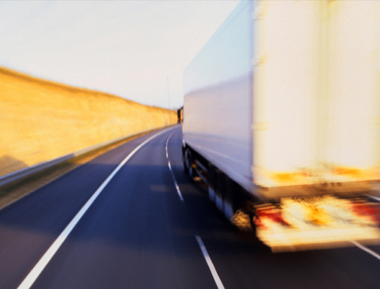 Image of white truck and trailer driving on highway, blurred to show motion