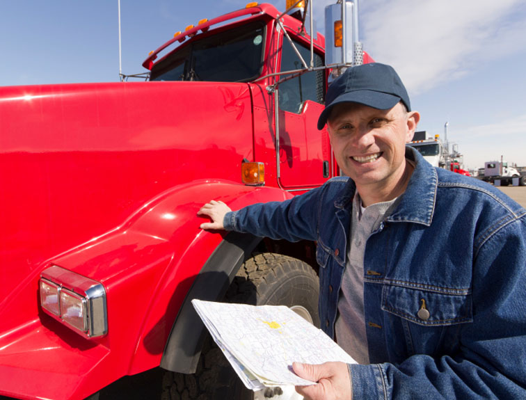 Image of truck driver standing with hand on red semi, holding a map and smiling.