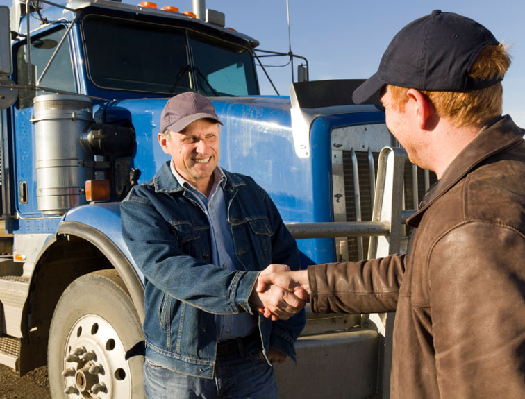Two men shaking hands with semi in the background.