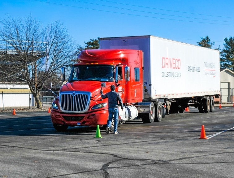 DriveCo semi truck parked in training yard with instructor walking nearby