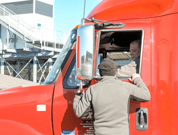 Man standing on door step of semi truck cab, looking into the window