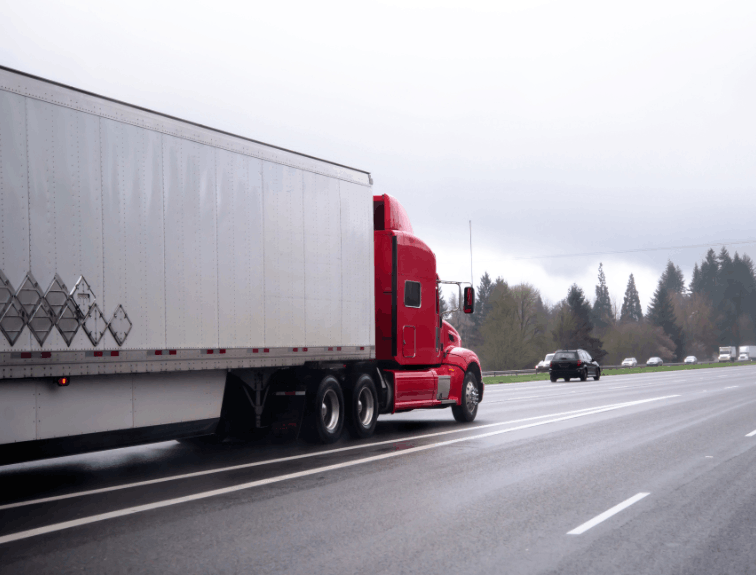 Red semi truck driving on highway, cars around it